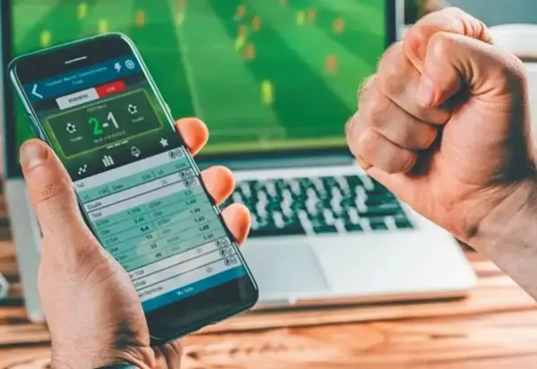Persona observando una apuesta deportiva en su celular y notebook.
